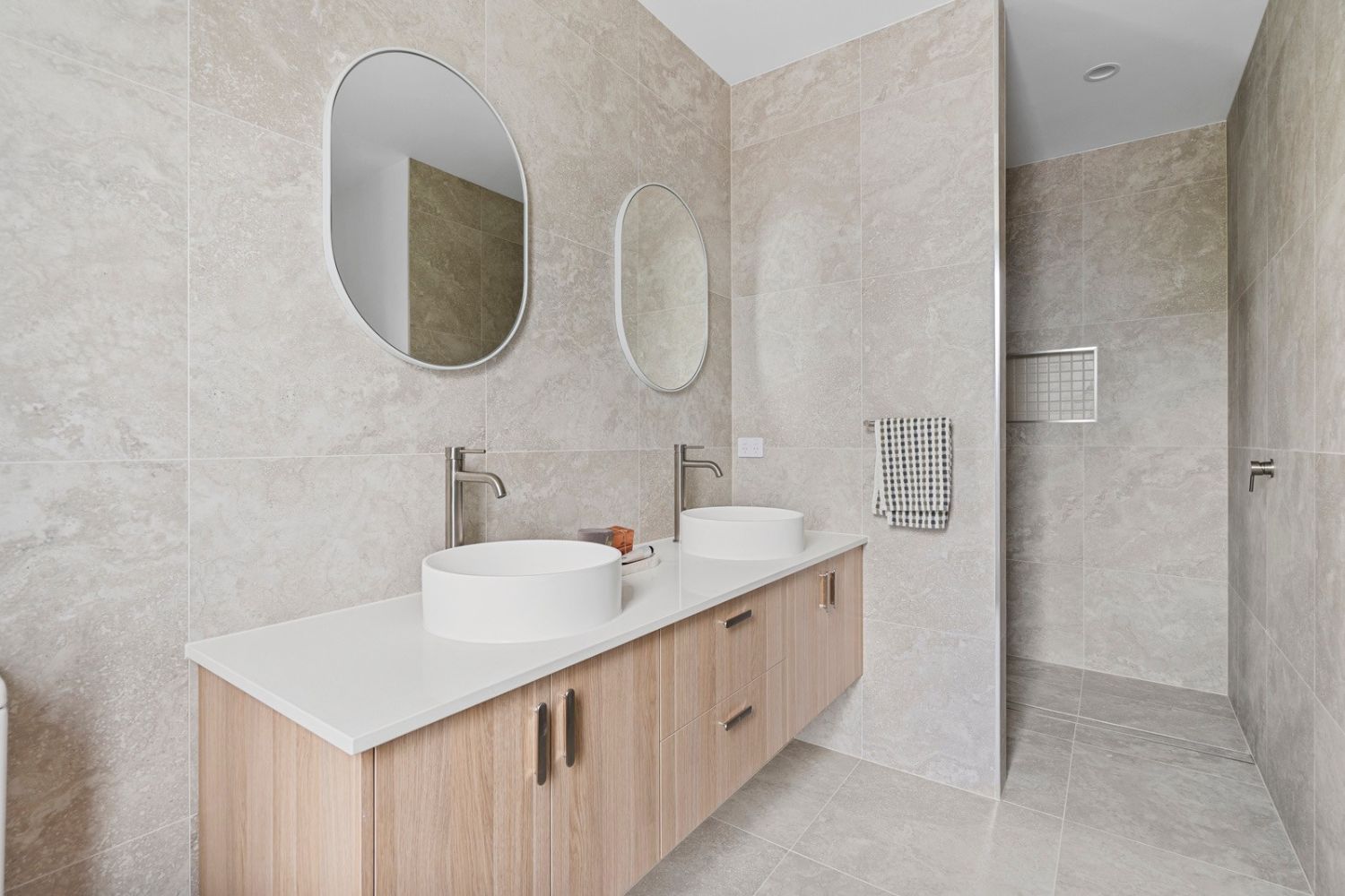 Twin vessel basins on a timber vanity beside a walk-in shower